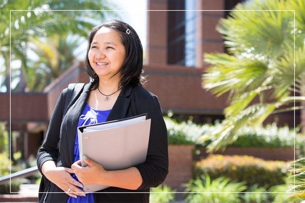 Woman walking outside a campus building holding a binder